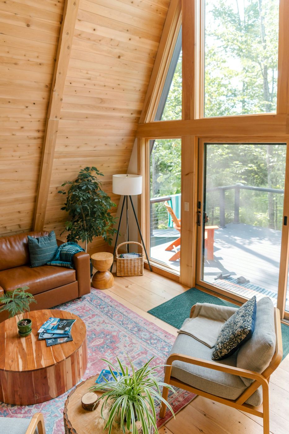 Sunlit A-frame cabin living room with a leather sofa and a deck through tall windows